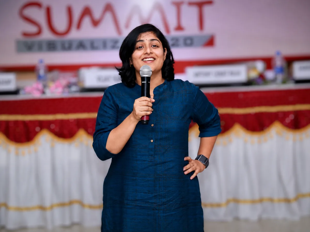 Sangeetha S Abishek early in her professional career, speaking with a microphone at a summit.
