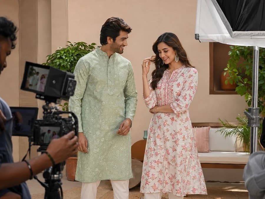Two actors in a scene on a lit set, with the camera and softbox in frame.