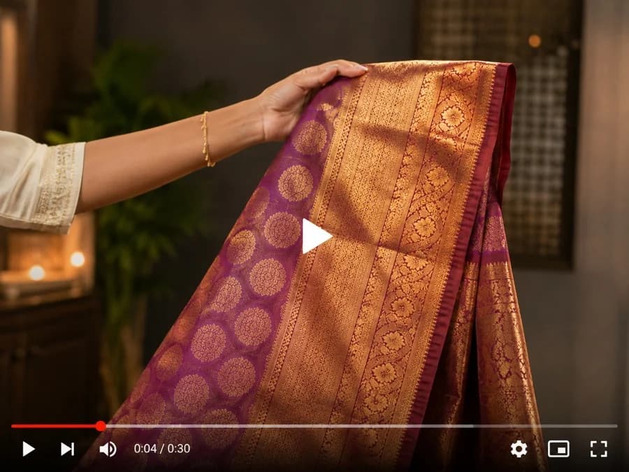 A hand unfurling a silk saree with a gold zari border, filmed close up as a product video.