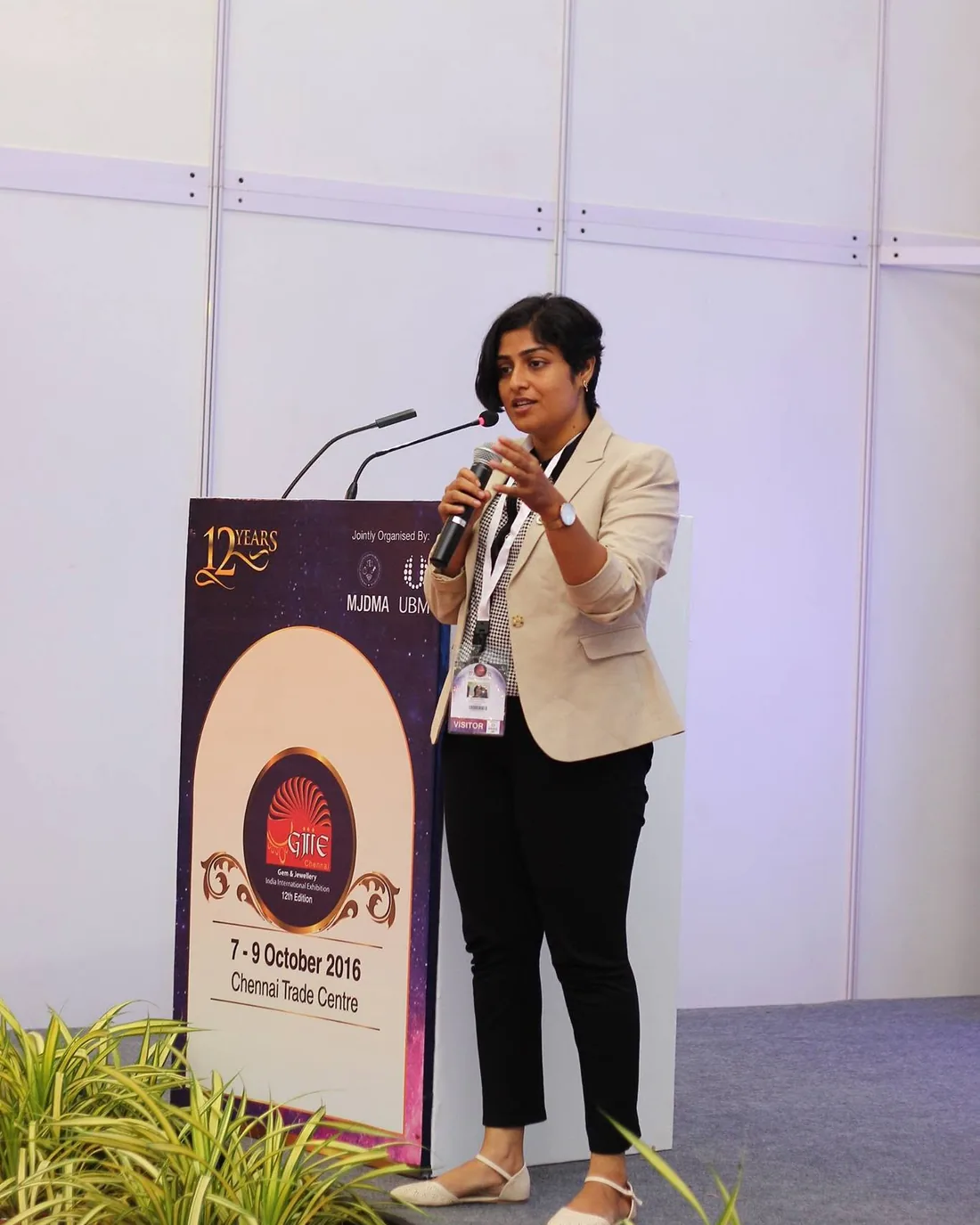 Sangeetha S Abishek speaking with a microphone at a lectern during an industry exhibition in Chennai.